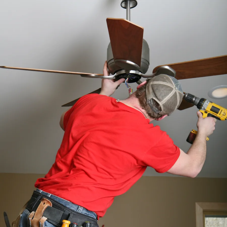 Technician connecting wiring at the canopy of a ceiling fan while holding a drill