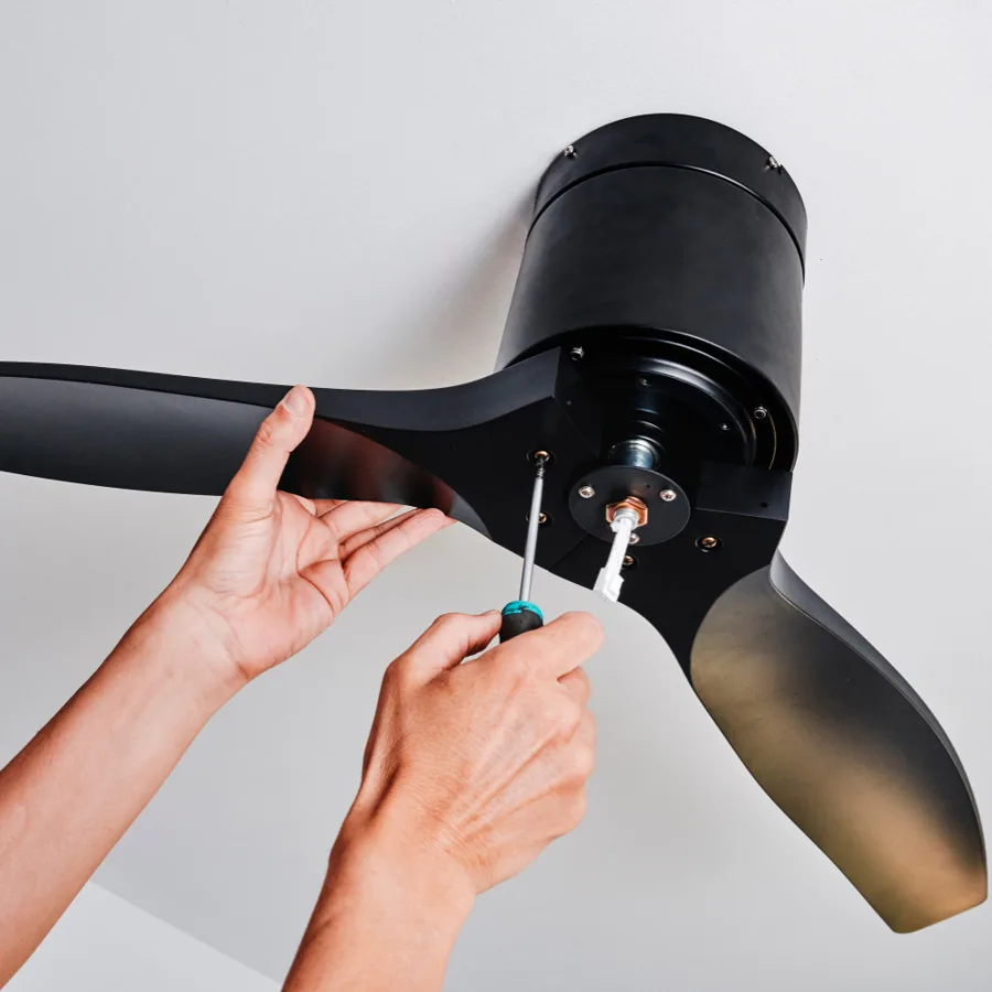 Hands attaching a blade to a black ceiling fan motor housing with a screwdriver