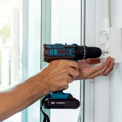 Electrician using a cordless drill to install an electrical outlet box on a wall
