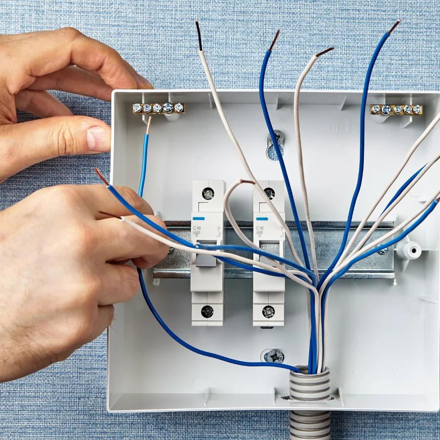 Hands connecting blue and white branch-circuit conductors to breakers inside an open electrical box