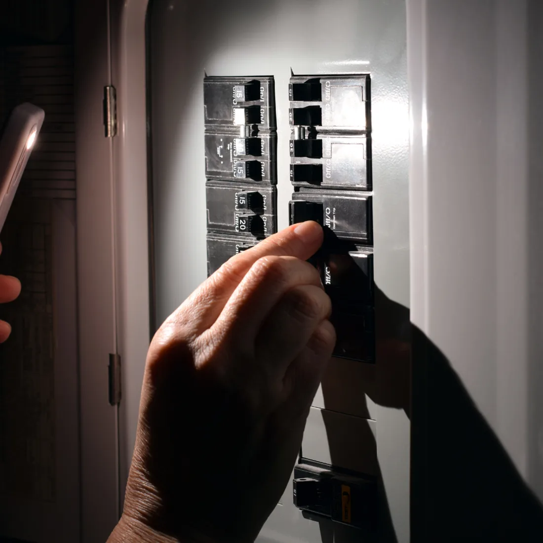 Hand switching a breaker inside an electrical panel lit by a flashlight