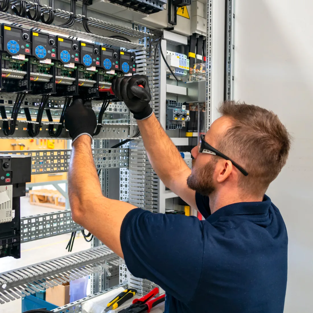 Electrician working at a control panel with indicator lights and rows of breakers