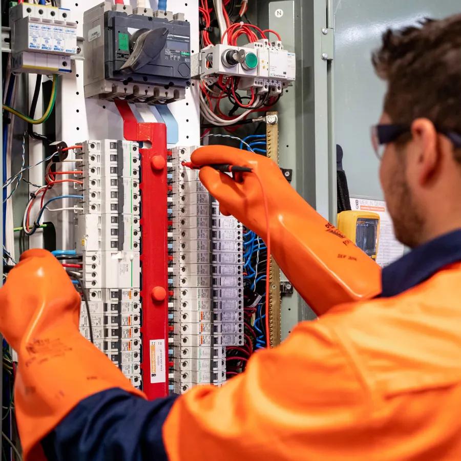 Electrician in protective gloves testing rows of breakers inside an electrical panel