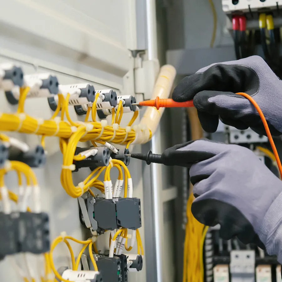 Gloved hands using test probes on yellow feeder conductors inside electrical distribution equipment