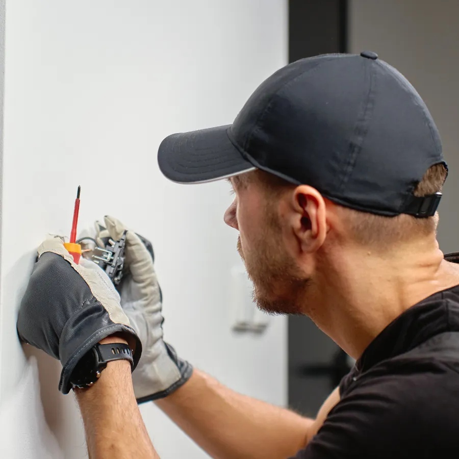 Electrician in work gloves using an insulated screwdriver on a wall-mounted electrical device