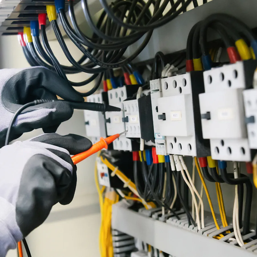 Electrician measuring voltage at contactors and terminals inside a control panel