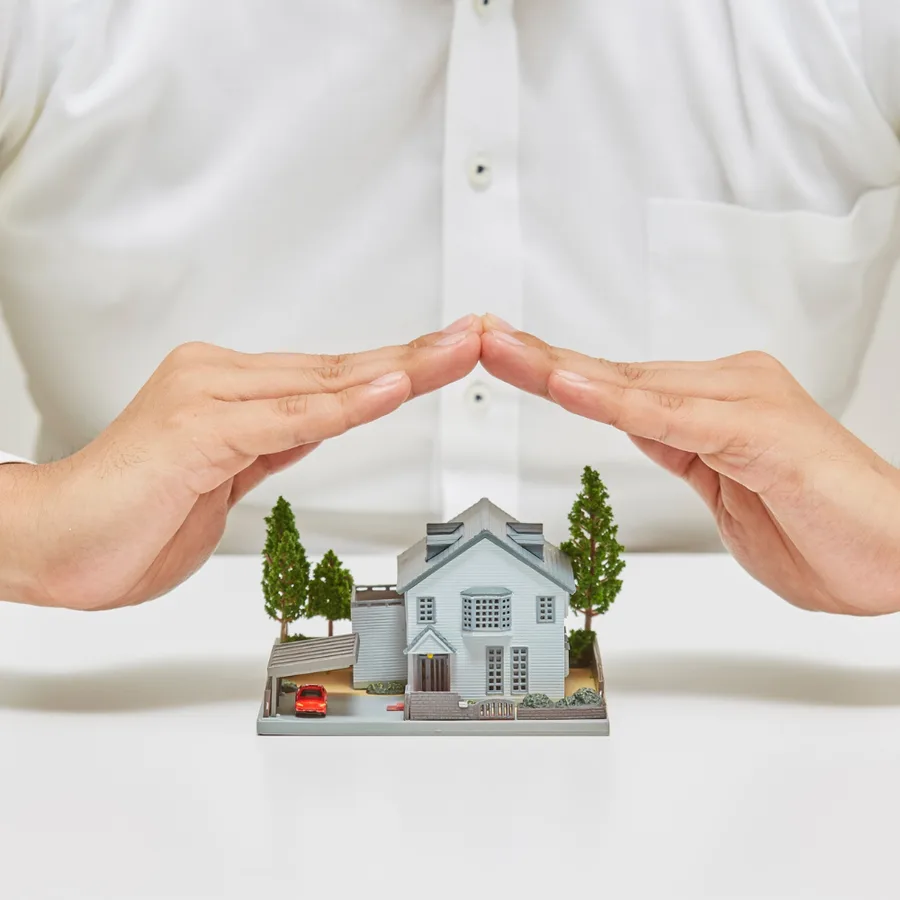 Person's hands sheltering a small model house on a white surface